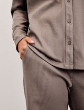 woman wearing a brown corduroy button down shirt and pants against a plain background.